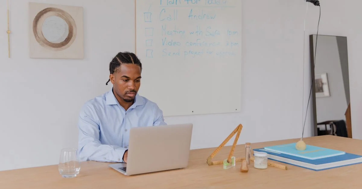 Un homme adulte en chemise bleue travaillant sur un ordinateur portable dans un bureau avec un tableau blanc.